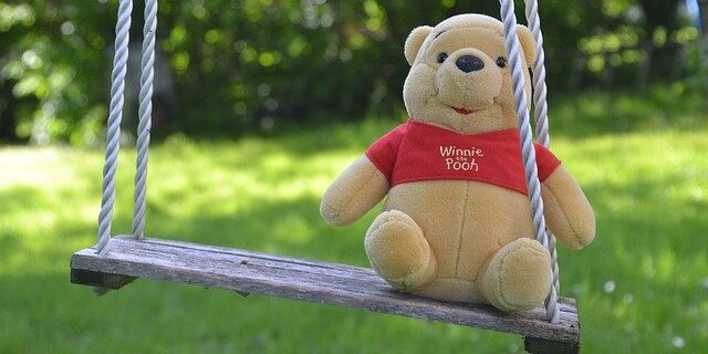 Winnie the Pooh stuffed animal on an outside swing